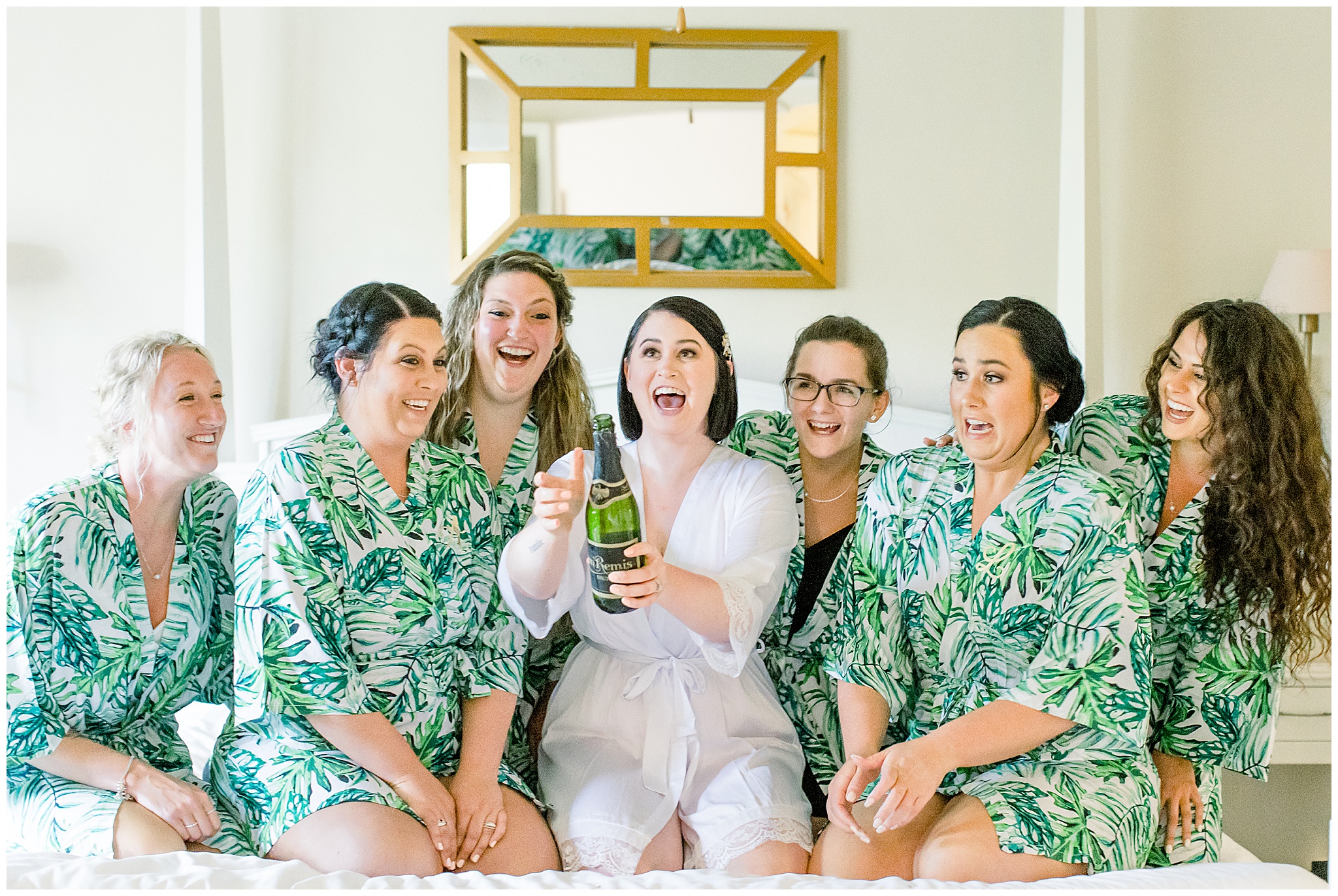 Bridesmaids and Bride in floral robes on bed, popping champagne